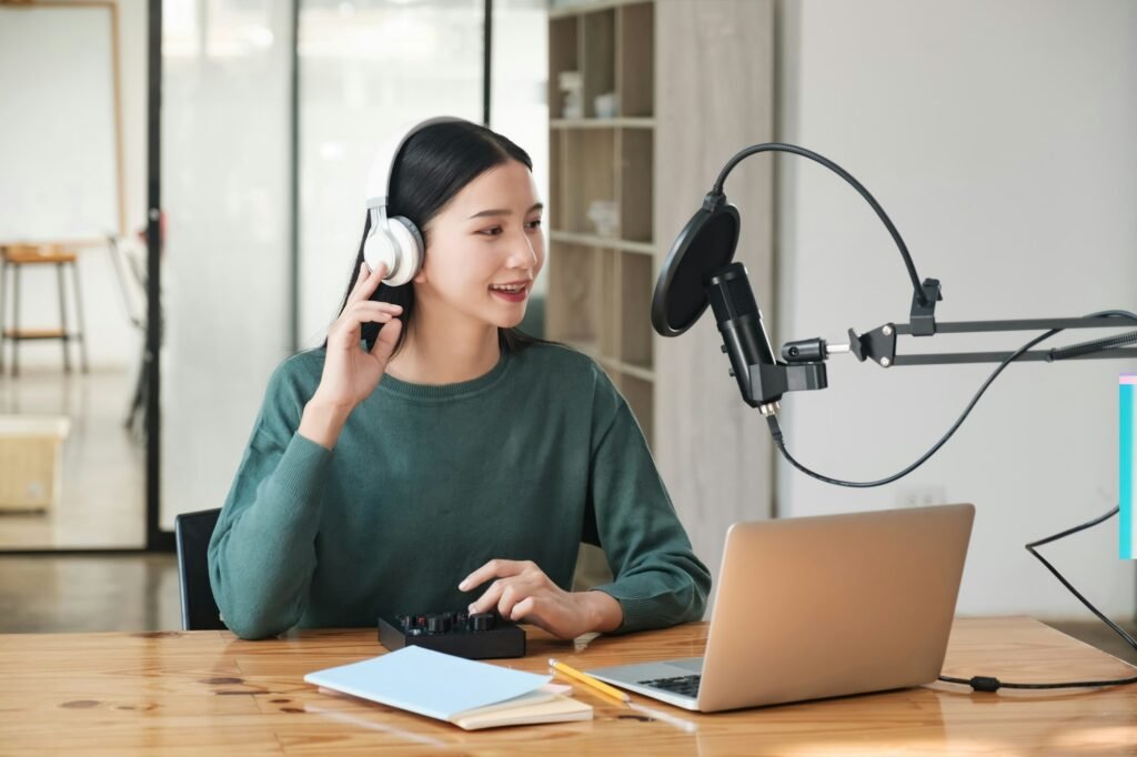 A woman is sitting at a desk with a laptop and a microphone