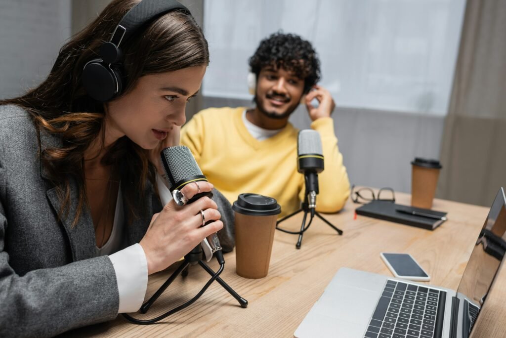 brunette radio host in headphones talking in professional microphone near laptop, smartphone