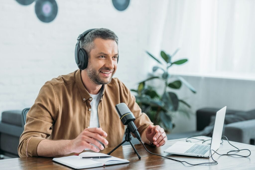 smiling radio host in headphones recording podcast in broadcasting studio